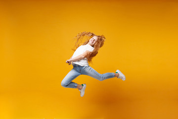 Fototapeta na wymiar Funny little ginger kid girl 12-13 years old in white t-shirt isolated on yellow background children portrait. Childhood lifestyle concept. Mock up copy space. Having fun, fooling around, jumping.