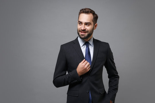 Smiling young bearded business man in classic black suit shirt tie posing isolated on grey background studio portrait. Achievement career wealth business concept. Mock up copy space. Looking aside.