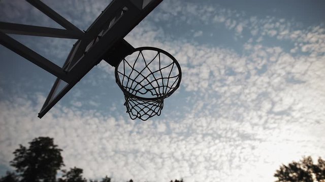 Low Angle View of Basketball Hoop and Men Hands Throwing and UnScoring at Partly Cloudy Sky Background. Healthy Lifestyle and Sport Concept. Slow Motion.