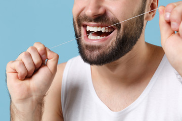 Close up cropped bearded young man in white shirt hold using dental floss isolated on blue pastel...