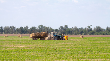 Tractor loading hay bales on truck agricultural works