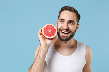 Bearded young man 20s years old in white shirt hold in hand half of grapefruit isolated on blue...