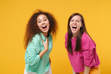 Fototapeta na wymiar Two laughing excited women friends european and african american girls in pink green clothes posing isolated on yellow orange background studio portrait. People lifestyle concept. Mock up copy space.