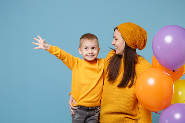 Fototapeta na wymiar Woman in yellow clothes have fun with cute child baby boy 4-5 years old celebrating birthday holiday party with colorful air balloons. Mommy son isolated on blue background. Family childhood concept.