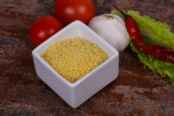 Raw couscous in the bowl served salad leaves, tomato and pepper