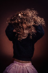 Studio portrait of little girl, a child playing with her long curly hair