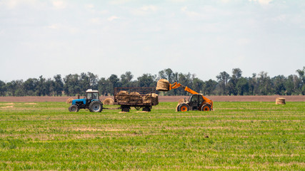 Tractor loading hay bales on truck agricultural works