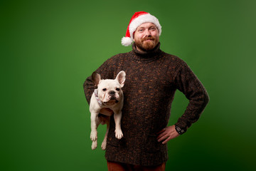 Smiling man in santa hat with bulldog on empty green background