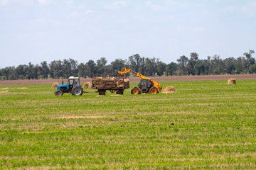 Tractor loading hay bales on truck agricultural works