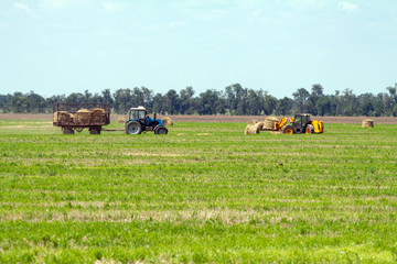 Tractor loading hay bales on truck agricultural works