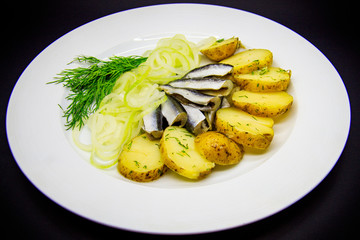 Sprat with baked potatoes on black background.