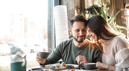Cute young couple is enjoying breakfast together. Modest romantic man and cute girl lowered their eyes