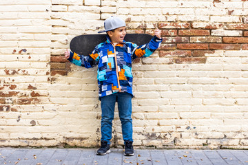 Fashion kid with his skateboard on a brick wall background