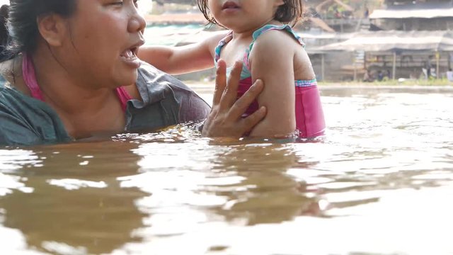 Little Asian baby girl holding on her auntie tight as she was afraid of staying in a water by herself and refused to try