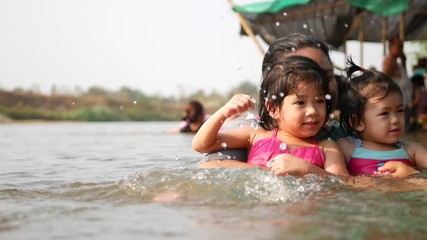 Two little Asian baby girls, sisters, enjoys playing water in a river with her auntie - playing outdoor and engaging with nature provides positive impact on baby's health and development