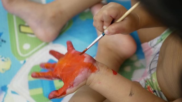 Hand of a little baby being painted with orange color - baby handprint / fingerprint painting