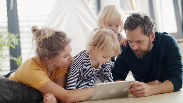 Young family with two small children indoors in bedroom, using tablet.
