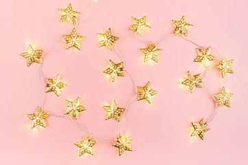 Christmas lights with golden stars glowing on soft light pastel pink background, pattern, top view.