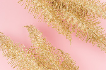 Gold and pink festive background - sparkling glittering fern branches on soft light pastel pink background, border, top view.