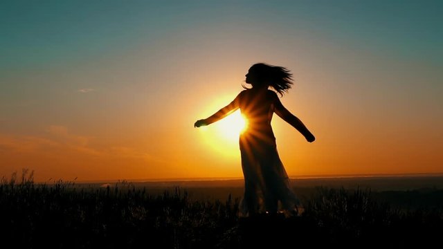 woman have fun enjoy freedom at sunrise silhouette of female in long skirt on the hill slow motion view on the sky with orange sun rays