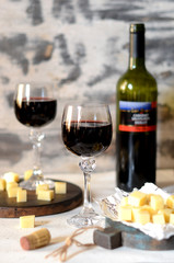 Red wine in glasses and cheese on a white wooden background