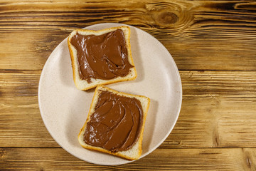 Two slices of bread with delicious chocolate hazelnut spread on wooden table. Top view