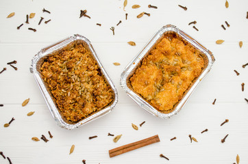 Indian food, fruit pies, subhadra and mithai, in foil plates on a white background, sprinkled with seeds, spices, cinnamon stick, top view