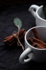 beautiful flat lay. cinnamon sticks and green leaves in a white cup on a dark background. 