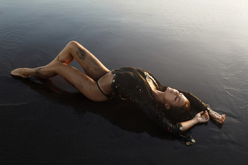 Sexy woman wearing black tunic is posing on the beach with black sand - Powered by Adobe