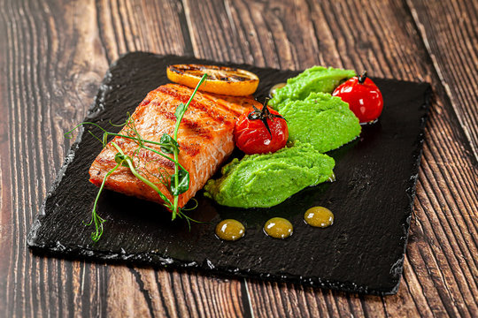 Spanish food concept. Fillet of red fish. Salmon steaks with spinach puree, with vegetables, on black slate. Background image. Copy space.