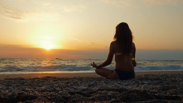 One young women practice yoga on a sandy beach by the sea or ocean at sunset. Self-knowledge and healthy lifestyle concept.
