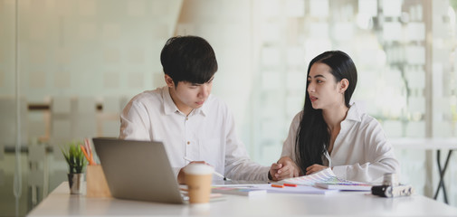 Two young professional graphic designer working on their project together with laptop computer in modern office