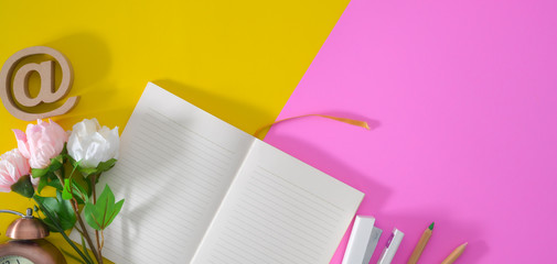 Top view of colourful workplace with open notebook and decorations on pink and yellow desk