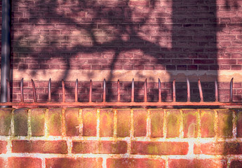 Element of a brick fence with metal spikes on a background of an old brick brown wall