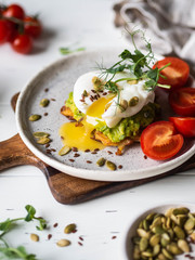 Healthy nutritious breakfast of potato pancake, mashed avocado, poached egg, pea sprouts and various seeds on ceramic plate