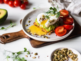 Healthy nutritious breakfast of potato pancake, mashed avocado, poached egg, pea sprouts and various seeds on a ceramic plate