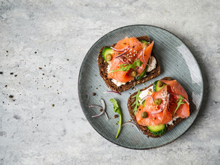Healthy toasts with rye bread with cream cheese, salmon, fresh cucumber, capers, sesame seeds, black pepper and arugula on plate. Top view