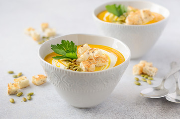 Pumpkin soup with cream, croutons, pumpkin seeds and parsley on a gray concrete or stone background.