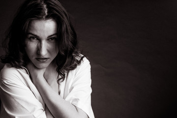 black and white photo of a brunette in a white shirt on a dark background who is choking herself...