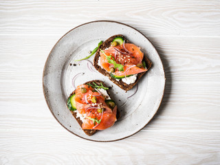 Healthy toasts with rye bread with cream cheese, salmon, fresh cucumber, capers, sesame seeds, black pepper and arugula on plate. Top view