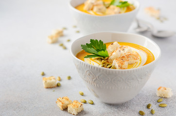 Pumpkin soup with cream, croutons, pumpkin seeds and parsley on a gray concrete or stone background.