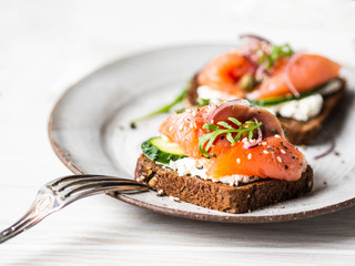 Healthy toasts with rye bread with cream cheese, salmon, fresh cucumber, capers, sesame seeds, black pepper and arugula