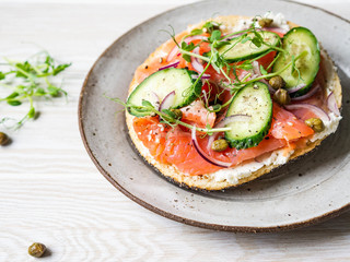 Healthy toast with cream cheese, salmon, fresh cucumber, capers, red onion, black pepper and pea sprouts on plate.
