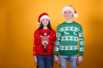 Fototapeta premium Studio portrait of young couple, boyfriend & girlfriend wearing santa claus hat & ugly christmas sweater. Holiday outfit w/ snowflake pattern print. Close up, copy space for text, isolated background.