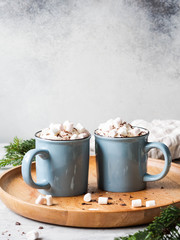 Two blue mugs with hot chocolate, whipped cream, chocolate chips on a wooden tray on a gray...