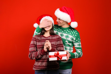 Studio portrait of young couple, boyfriend & girlfriend wearing santa claus hat & ugly christmas sweater. Holiday outfit w/ snowflake pattern print. Close up, copy space for text, isolated background.