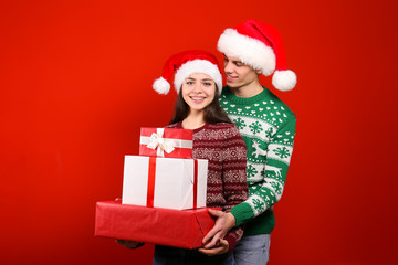 Studio portrait of young couple, boyfriend & girlfriend wearing santa claus hat & ugly christmas sweater. Holiday outfit w/ snowflake pattern print. Close up, copy space for text, isolated background.