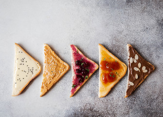 Various sweet toasts with chocolate paste, condensed milk, peanut butter and fruit apricot jam, sprinkled with sesame seeds, almond flakes and fresh thyme. Top view. Copy space