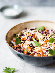 Red cabbage, carrot, cabbage coleslaw salad in blue bowl on grey background.