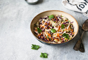 Red cabbage, carrot, cabbage coleslaw salad in blue bowl on grey background.